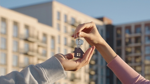 two people exchanging house-shaped keychain with keys outside residential building